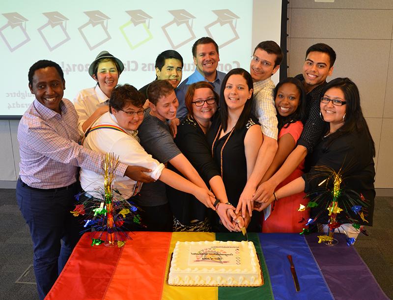 Rainbow graduates cutting a cake together.